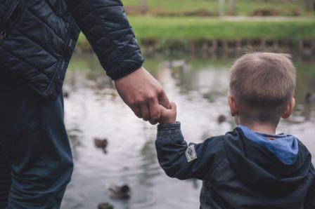 Boy holding an adults hand looking at a pond